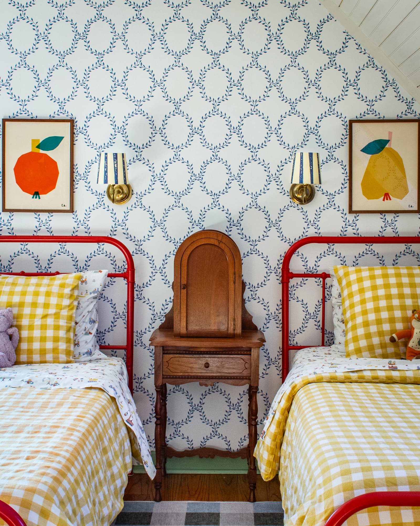 Red twin beds in a child's bedroom with colorful art above each. An antique phone cabinet sits between the two beds