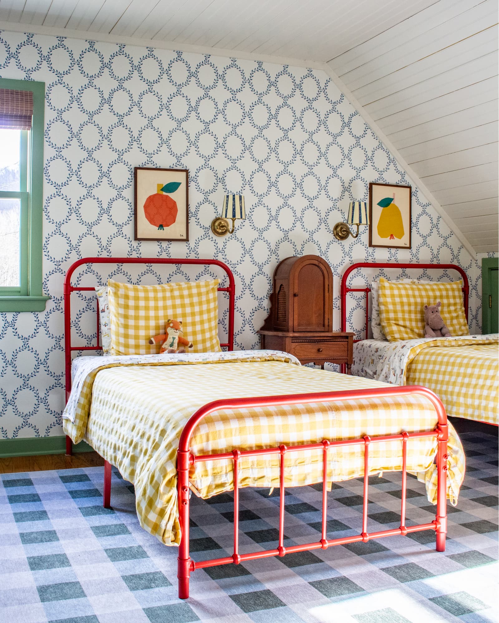 Red twin beds in a child's bedroom with colorful art above each. An antique phone cabinet sits between the two beds
