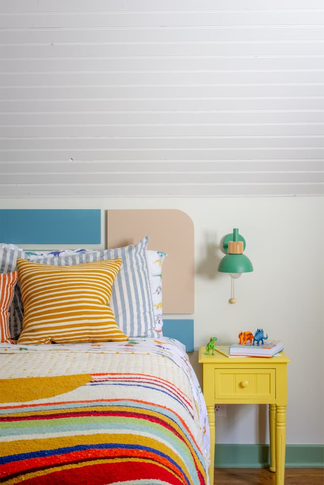 Colorful bed in a kids room with green reading sconce, and a yellow nightstand.