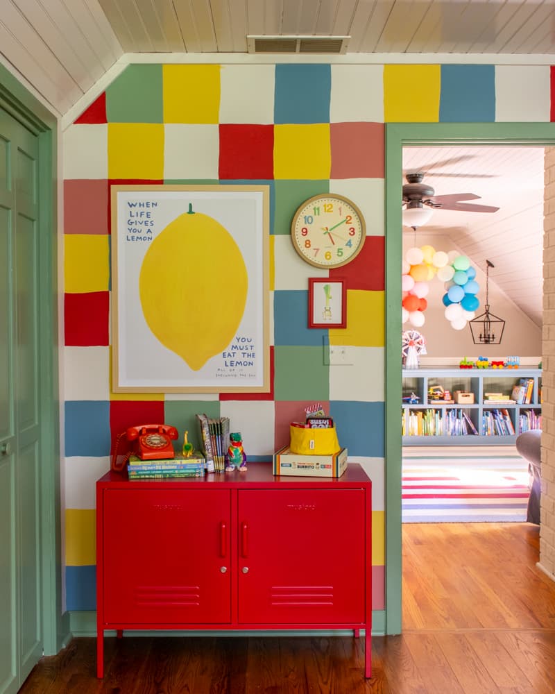 Checkered wall in a colorful kids bedroom with a lemon print, colorful clock and a red cabinet.