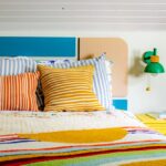 Queen bed in a colorful kids room with a green sconce and yellow nightstand.