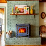 Painted green brick fireplace with a blue stove in the middle. The mantle is full of colorful artwork and decor