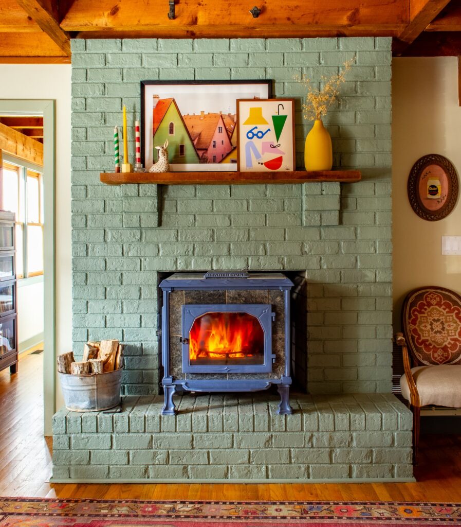 Painted green brick fireplace with a blue stove in the middle. The mantle is full of colorful artwork and decor