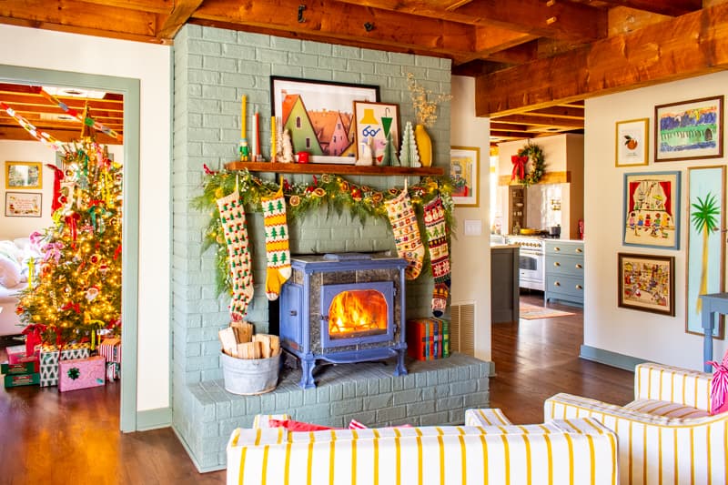 Fireplace in a home decorated for Christmas with garland and stockings. A tree from the other room is visible in the background
