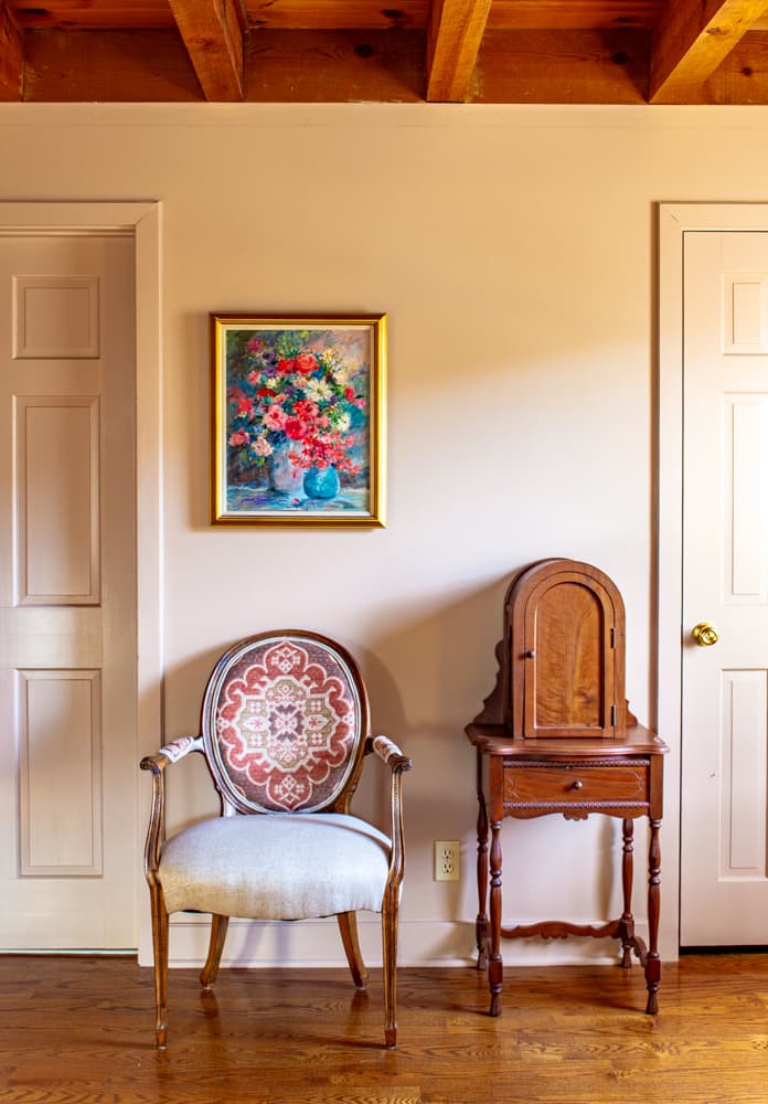 Chair and antique telephone cabinet under a painting of colorful flowers.
